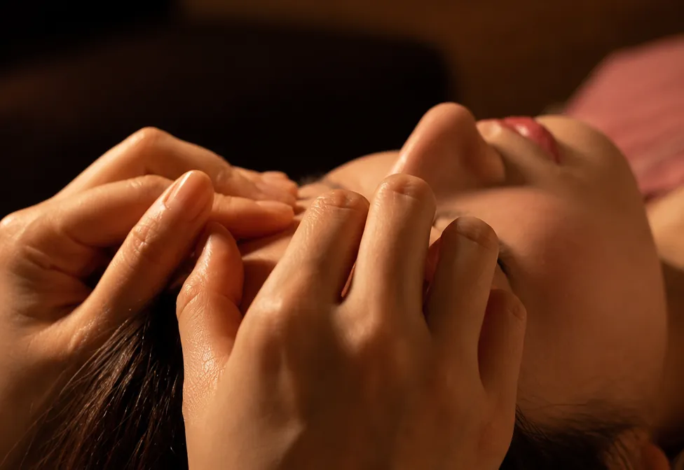 Hands massaging a guest’s temples as they rest with eyes closed